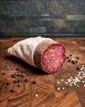 A sliced Air Dried Salami wrapped in a beige cloth, placed on a wooden surface
