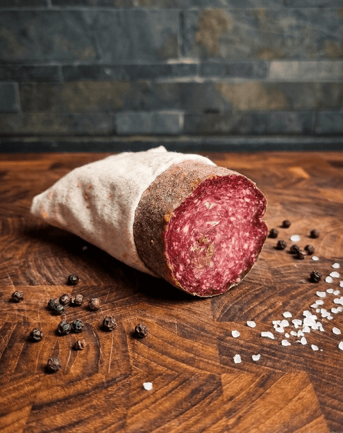 A sliced Air Dried Salami wrapped in a beige cloth, placed on a wooden surface