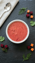 A white bowl filled with a Borscht soup, arranged on a dark slate surface.