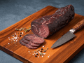 A sliced Bündnerfleisch and several cut slices rest on a wooden cutting board