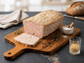 A loaf of Coarse Meatloaf with a sliced piece on a wooden cutting board