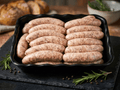 Fresh Bratwurst arranged in a black rectangular tray on a dark stone surface
