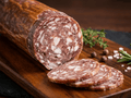 A sliced log of Genoa Wine Salami on a wooden board, with several round slices placed in front