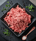 Raw Ground Pork piled in a square black dish on a dark stone surface
