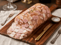 A large log of Headcheese displayed on a wooden serving board