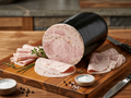 A large cut of Herbed Ham Sausage on a wooden cutting board