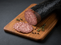 A sliced Hungarian Salami resting on a wooden cutting board with three round slice placed in front