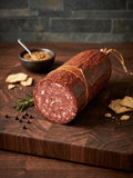 A sliced log of Italian Wine Salami, displayed on a dark wooden cutting board