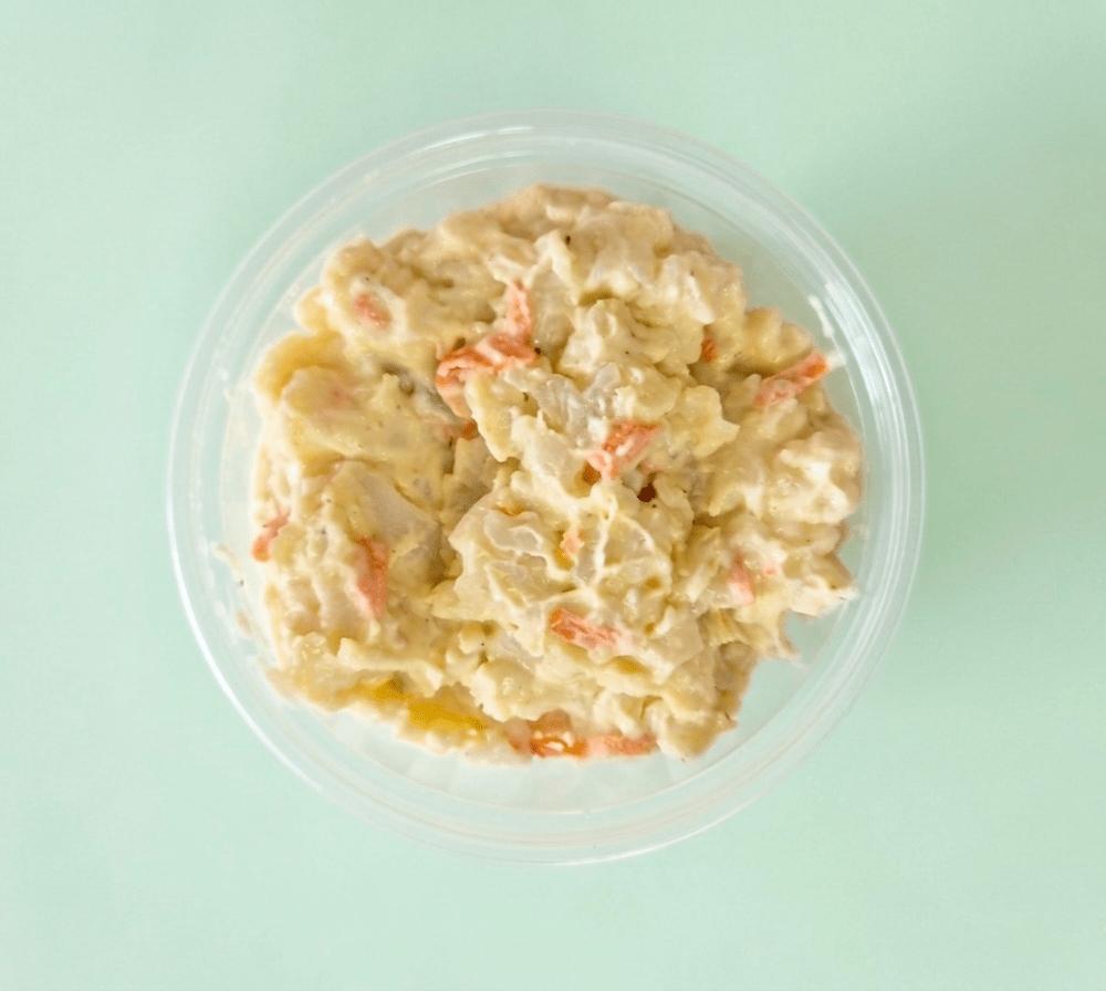 Creamy potato salad with visible orange carrot pieces, served in a clear round plastic container