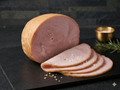 A sliced Smoked Turkey Breast with several thin slices arranged in front on a dark stone serving board