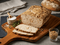 A loaf and two slices of Tuscan Meatloaf on a wooden cutting board