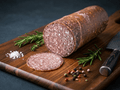 A sliced log of Westfalian Salami resting on a wooden cutting board, with a round slice placed in front
